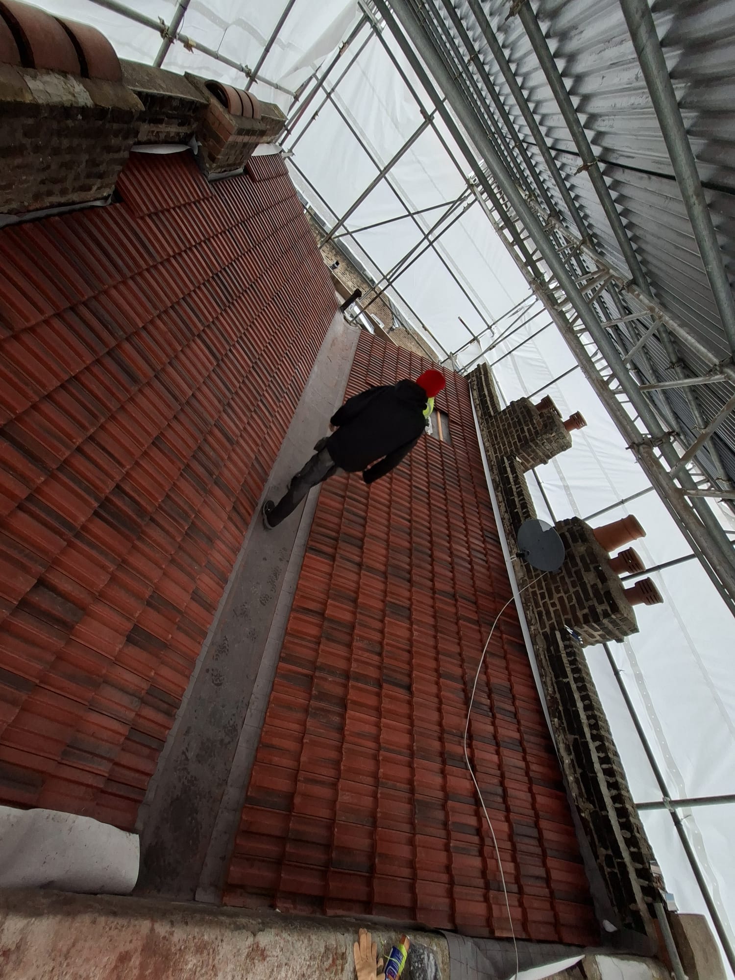 Roofer installing clay tiles on new roof in North London